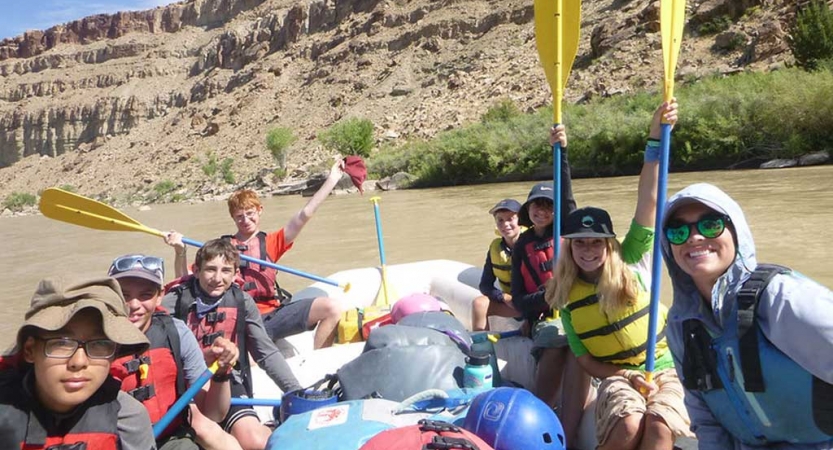 a group of students smile and raise paddles in the air while rafting on an outward bound trip